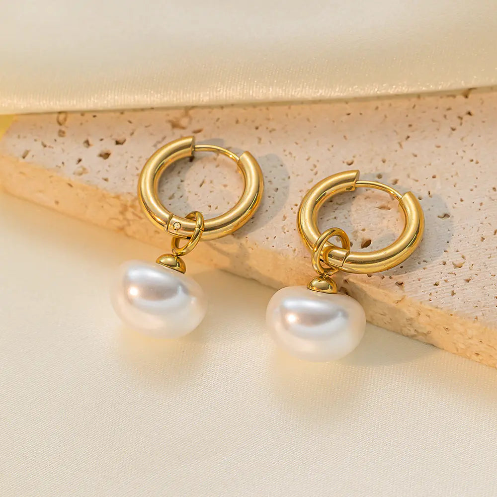 Gold hoop earrings with pearl drops on a beige surface