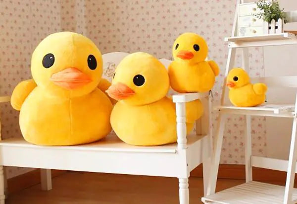 Four yellow rubber duck plush toys on a white bench in a room with floral wallpaper.