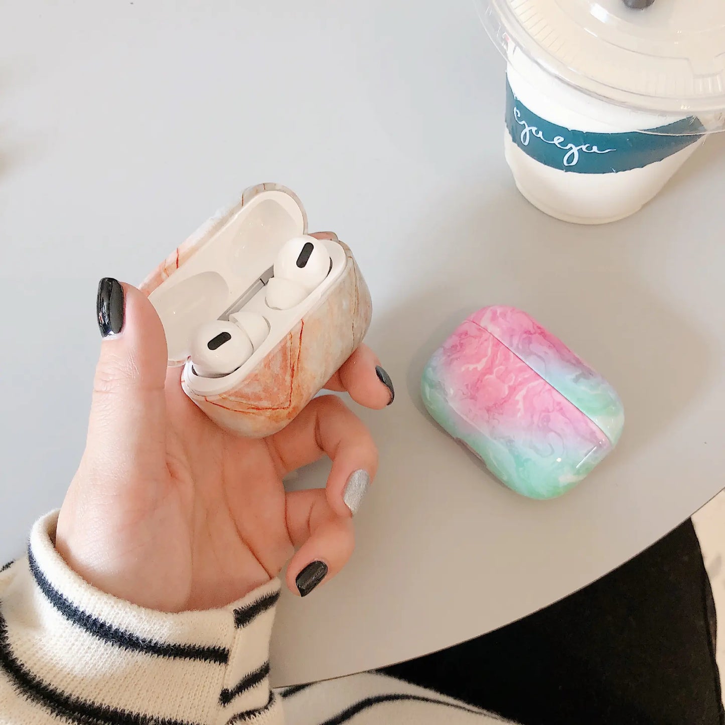 Hand holding a white airpod case with pink and green marble design on a light surface.