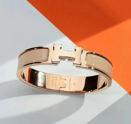 Rose gold bracelet with a prominent 'H' logo on a white and orange background