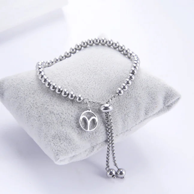 Silver beaded bracelet with a pendant on a white pillow