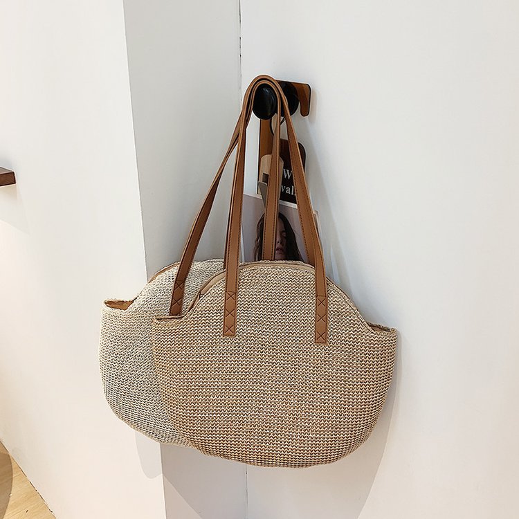 Woven handbag with brown straps hanging on a hook against a white wall.