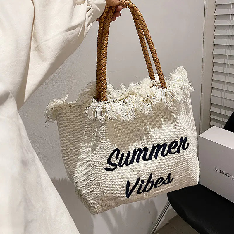 Beige tote bag with 'Summer Vibes' text held by a person, with a plain background.