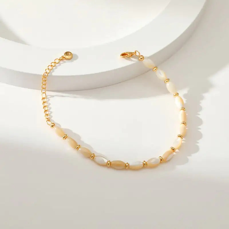 Beige shell-pearl bracelet with 18K gold clasp displayed on sunlit white background