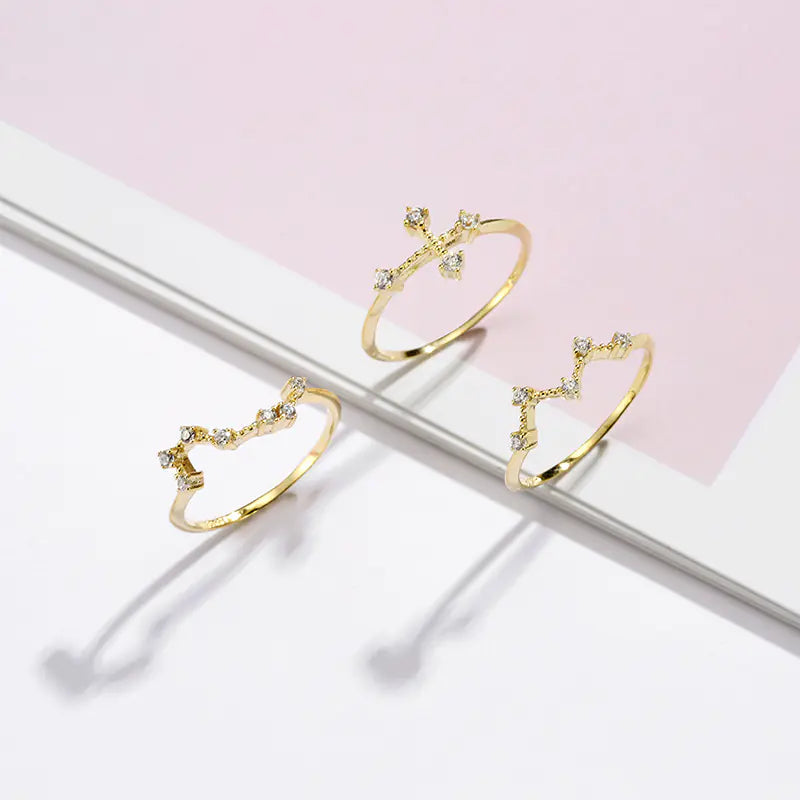 Three gold rings with gemstones on a light pink and white background