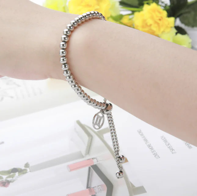 Silver beaded bracelet on a wrist with a blurred background of flowers and text.