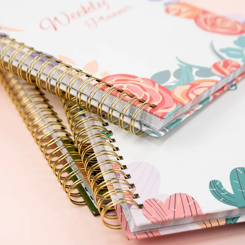 Two spiral-bound planners with floral and cactus designs on a light pink background