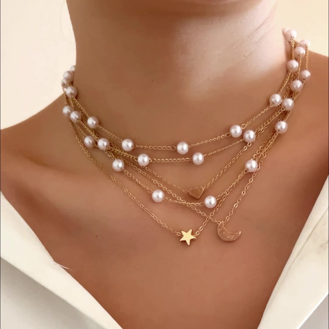 Multiple pearl necklaces with star and moon pendants on a person's neck against a neutral background
