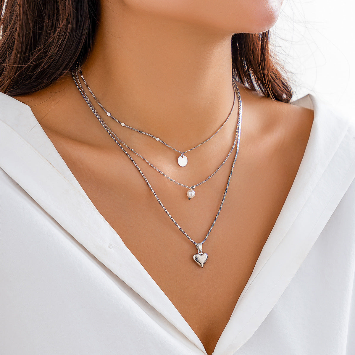 Close-up of a woman wearing multiple necklaces with heart and pearl pendants on a white background