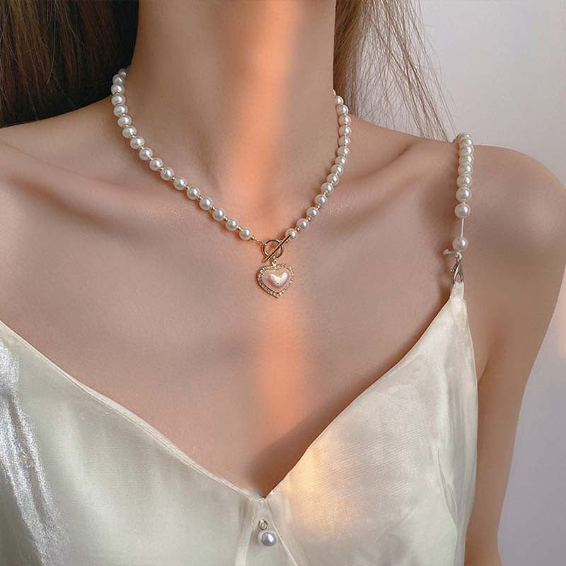 Pearl necklace with a heart pendant worn by a person in a light green top.