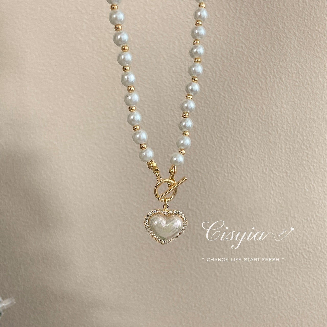 Pearl necklace with a heart-shaped pendant on a beige background, featuring the brand 'Cisyia'.