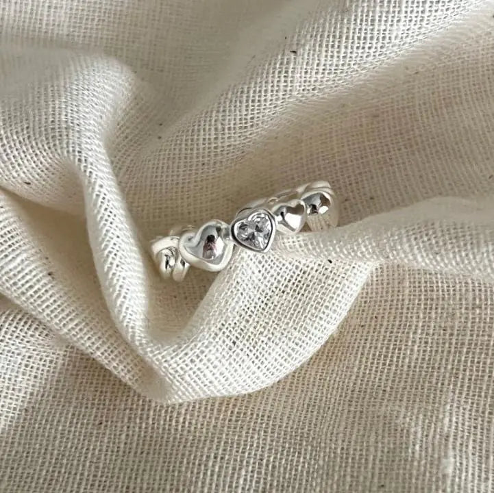 Silver ring with heart designs on a beige fabric background