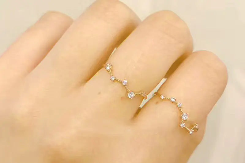 Gold ring with small stones on a hand against a beige background