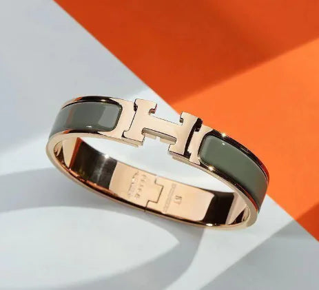 Gold and black bracelet with a prominent 'H' on a white and orange background