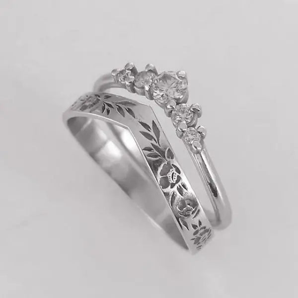 Silver ring with floral engraving and diamond accents on a light gray background