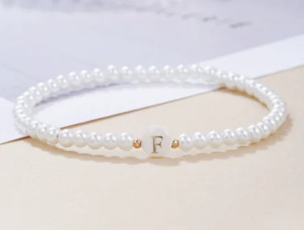 Pearl bracelet with a gold letter 'F' charm on a light background