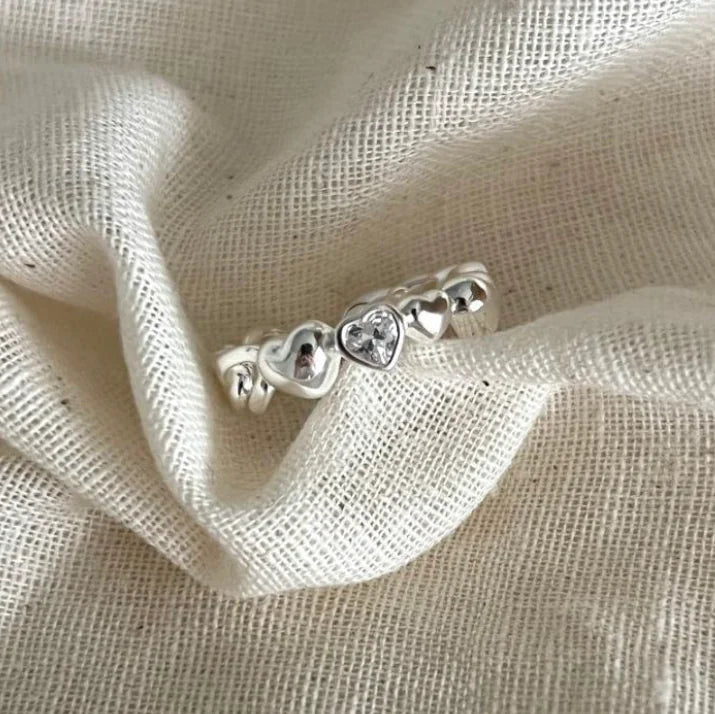 Silver ring with heart-shaped stones on a beige fabric background