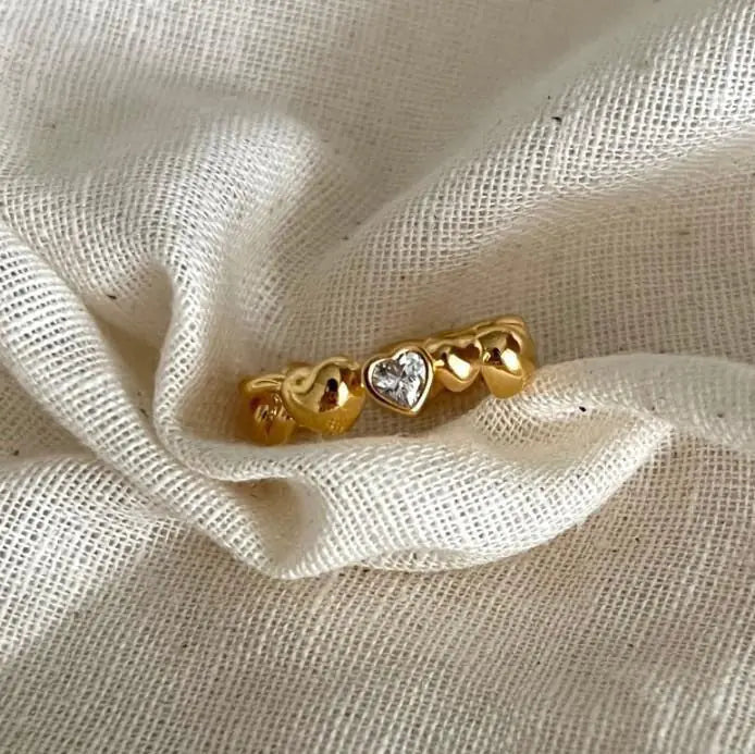 Gold ring with heart designs on a textured beige fabric background