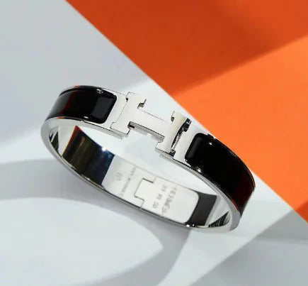 Silver bracelet with black strap on a white and orange background
