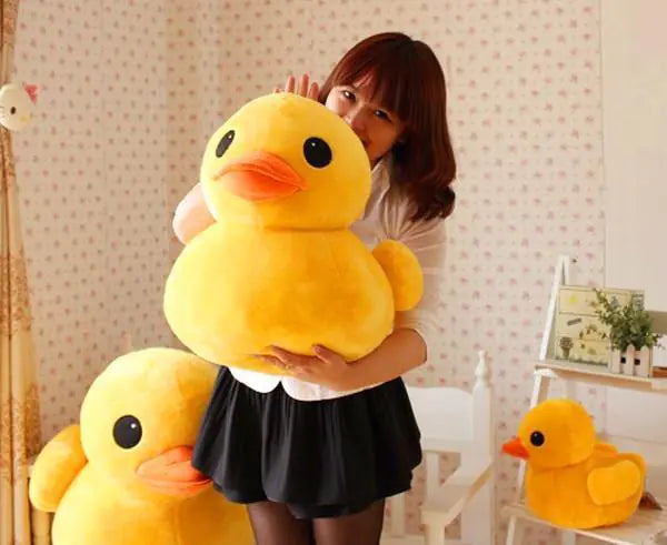 Person holding a large yellow plush duck toy in a room with patterned wallpaper.