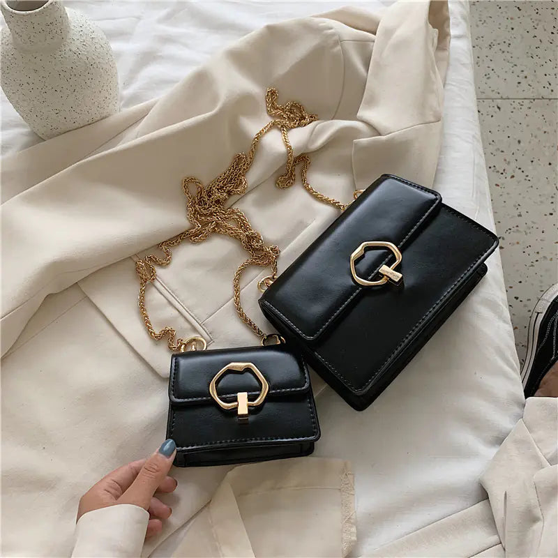 Two black handbags with gold hardware on a light-colored surface.
