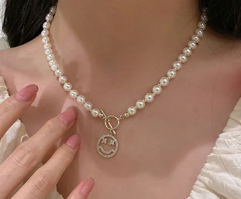 Pearl necklace with a smiley face charm worn by a person