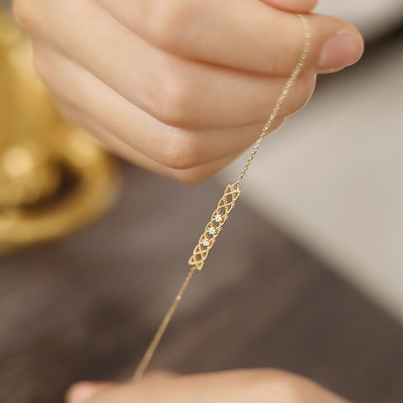 Gold necklace with diamond accents held by a hand against a blurred background