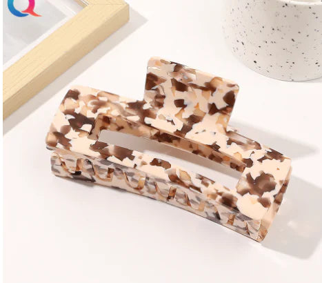 Marbled patterned hair clip on a white surface with a blurred background