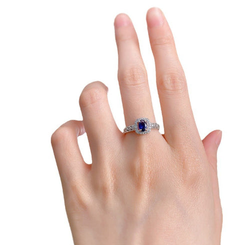 Silver ring with a blue gemstone on a hand against a white background