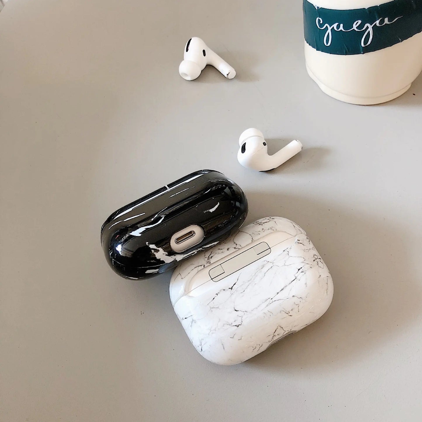 Wireless earbuds with marble-patterned case on a light gray surface