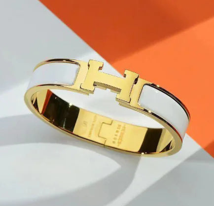 Gold bracelet with a prominent 'H' logo on a white and orange background