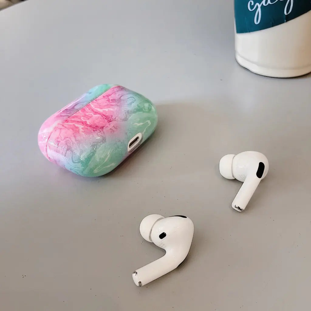 White wireless earbuds with a colorful marble case on a gray surface.