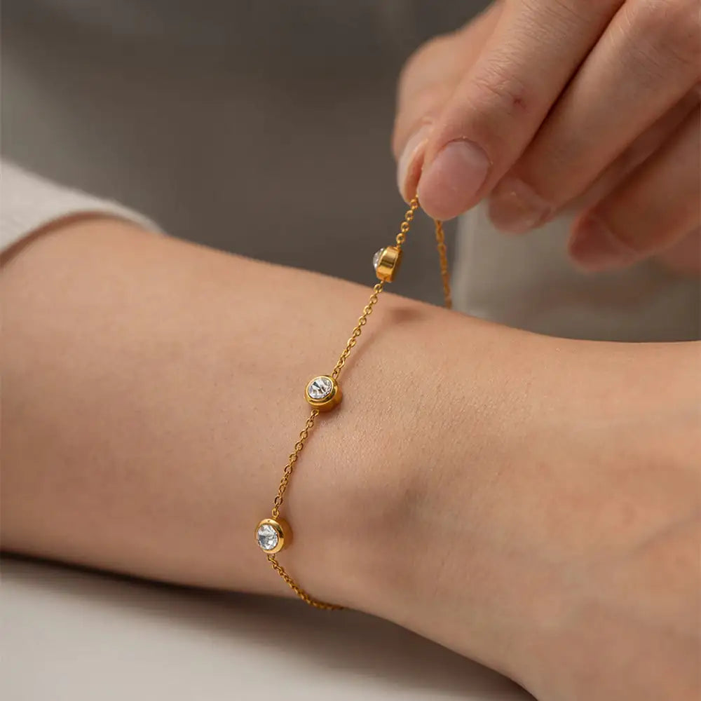 Close-up of an 18K gold-plated stainless-steel bracelet with a single round zircon stone on a neutral background.