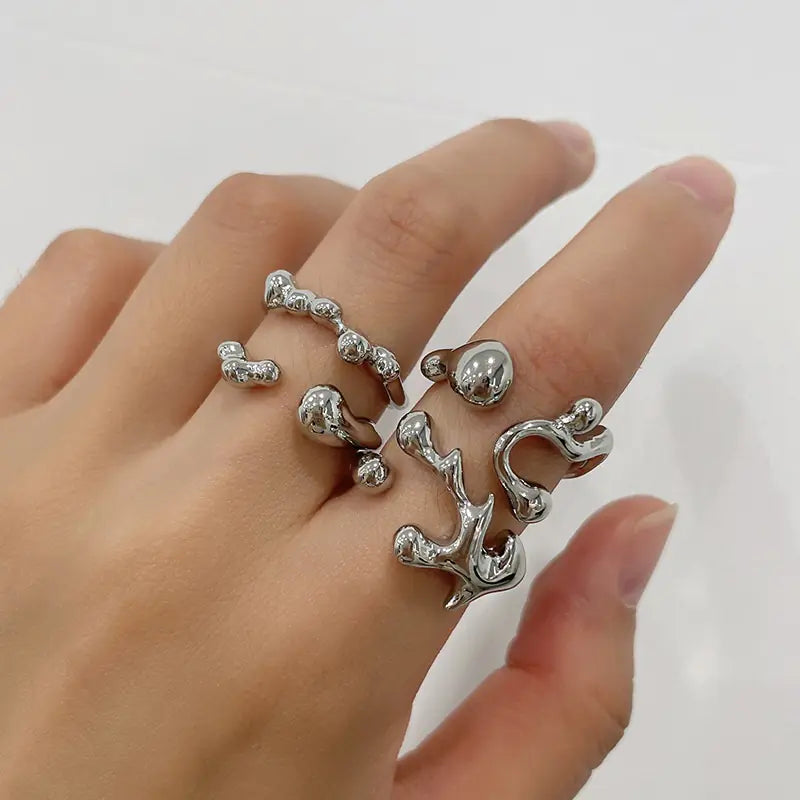 Hand wearing multiple silver rings on a plain background