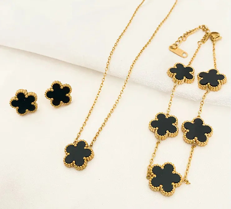 Gold necklace and earrings with black clover-shaped pendants on a white background