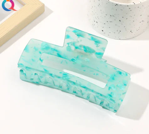 Turquoise and white marbled hair clip on a white surface with a blurred background