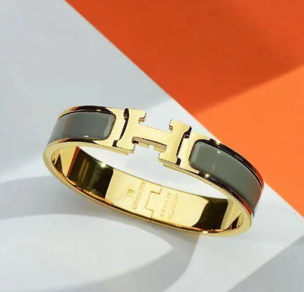 Gold bracelet with black accents on a white and orange background