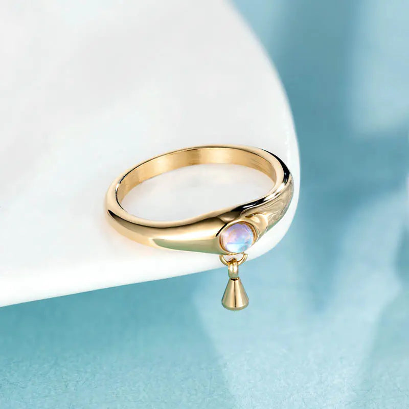 Gold ring with a gemstone and teardrop pendant on a light blue background