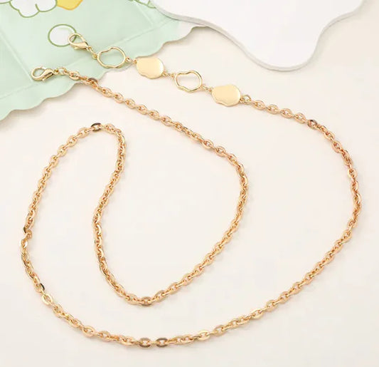 Gold chain necklace on a white surface with a light green floral-patterned napkin.