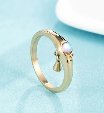 Gold ring with a small gemstone and pendant on a light blue background