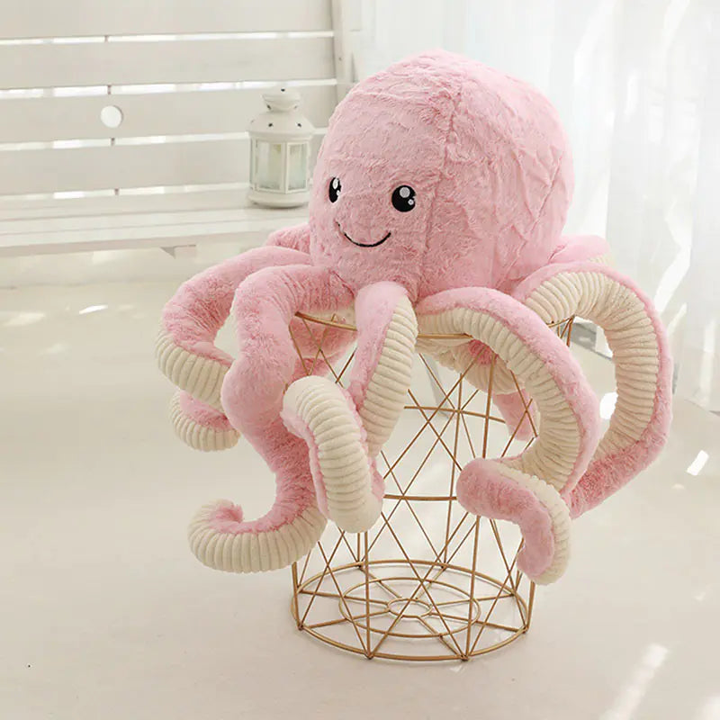 Pink plush octopus toy on a gold wire basket with a white background