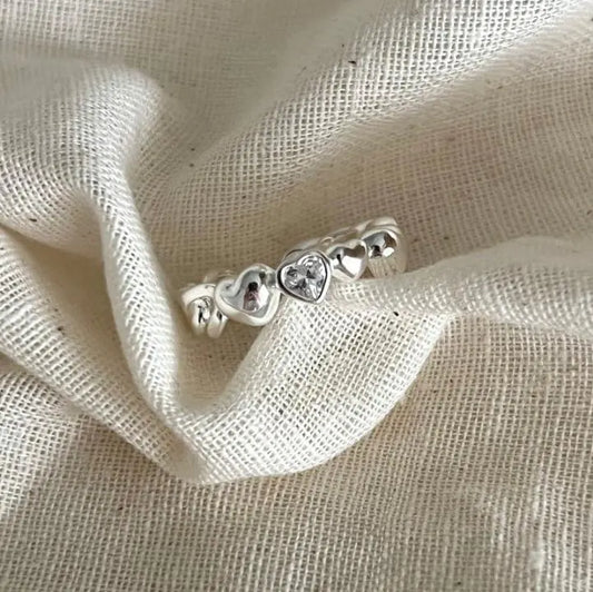 Silver ring with heart designs on a beige fabric background