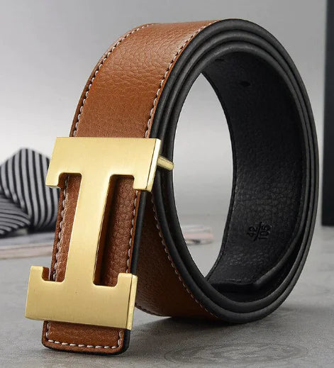 Brown and black leather belt with gold 'T' buckle on a gray surface.