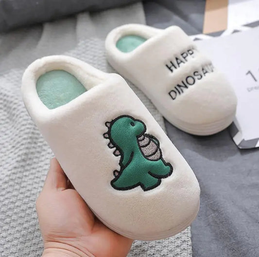 White slippers with a green dinosaur design held by a hand on a gray surface.