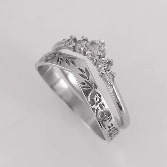 Silver ring with floral engraving and diamond accents on a light gray background