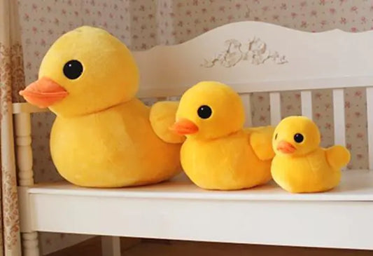 Three yellow rubber duck plush toys on a white surface with a floral-patterned wall in the background.